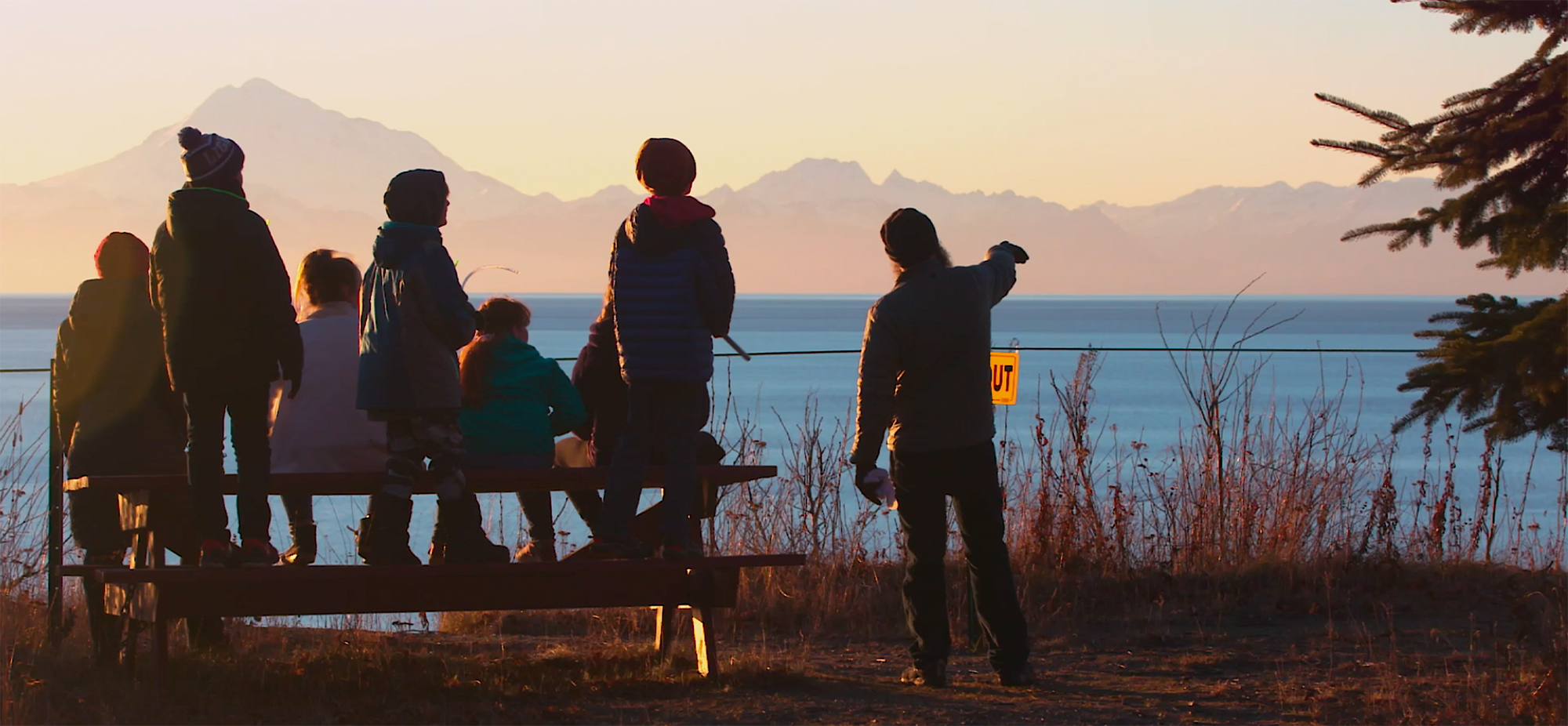 People sitting on a bench and looking at a lake and sunset