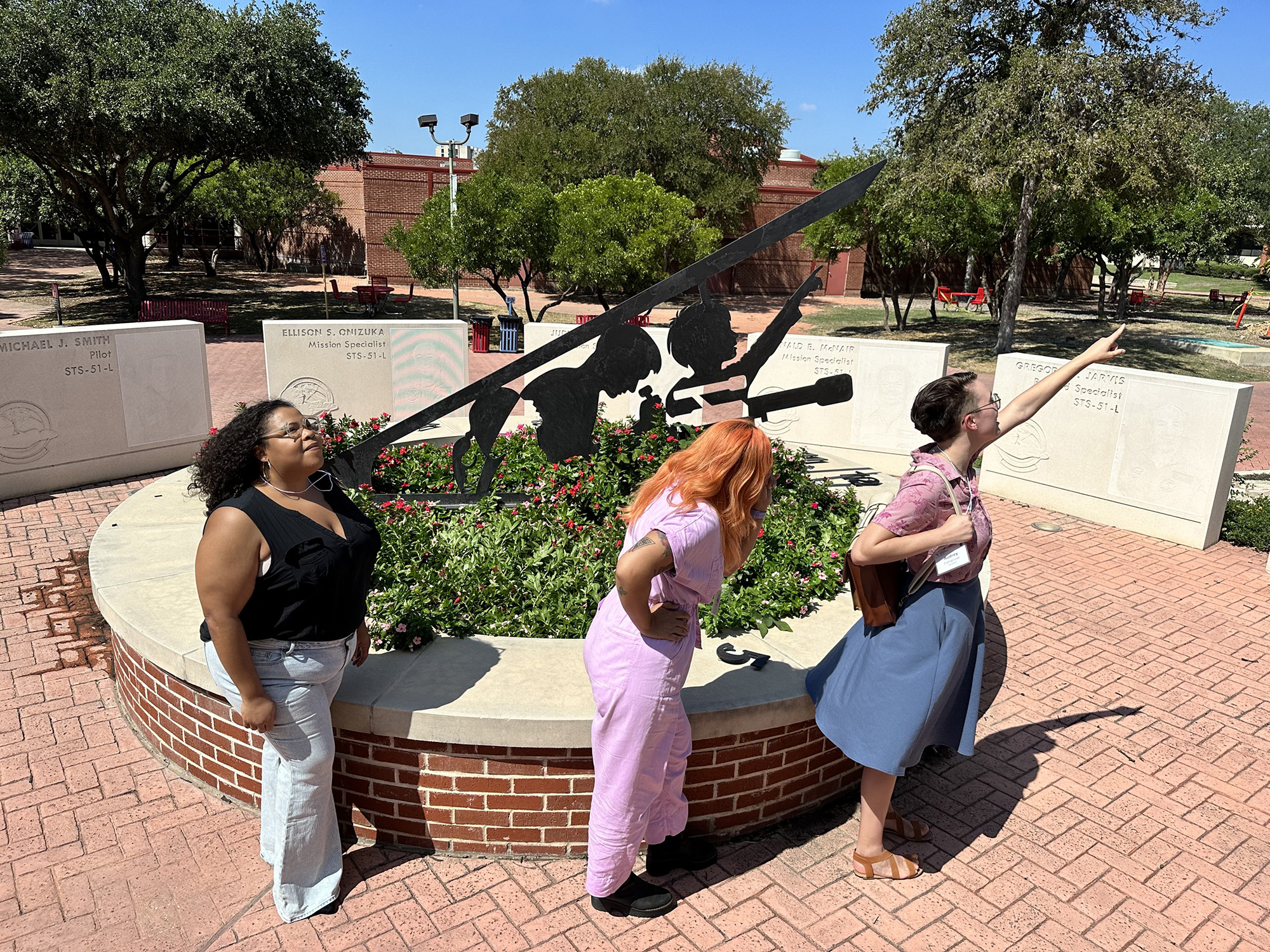 Three people standing in a line and pointing to the sky