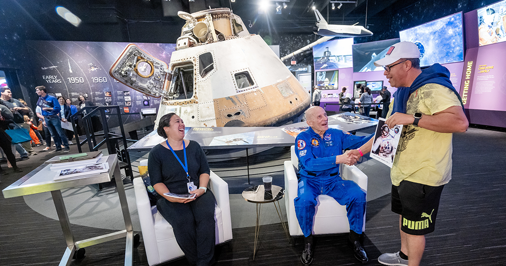 Two people sitting and one standing by a front part of a space ship